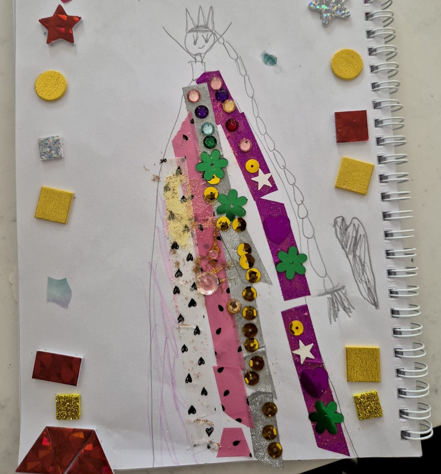A phone photo of a child's drawing of a queen in a sequinned dress, taped and glittered onto a sketchbook page.