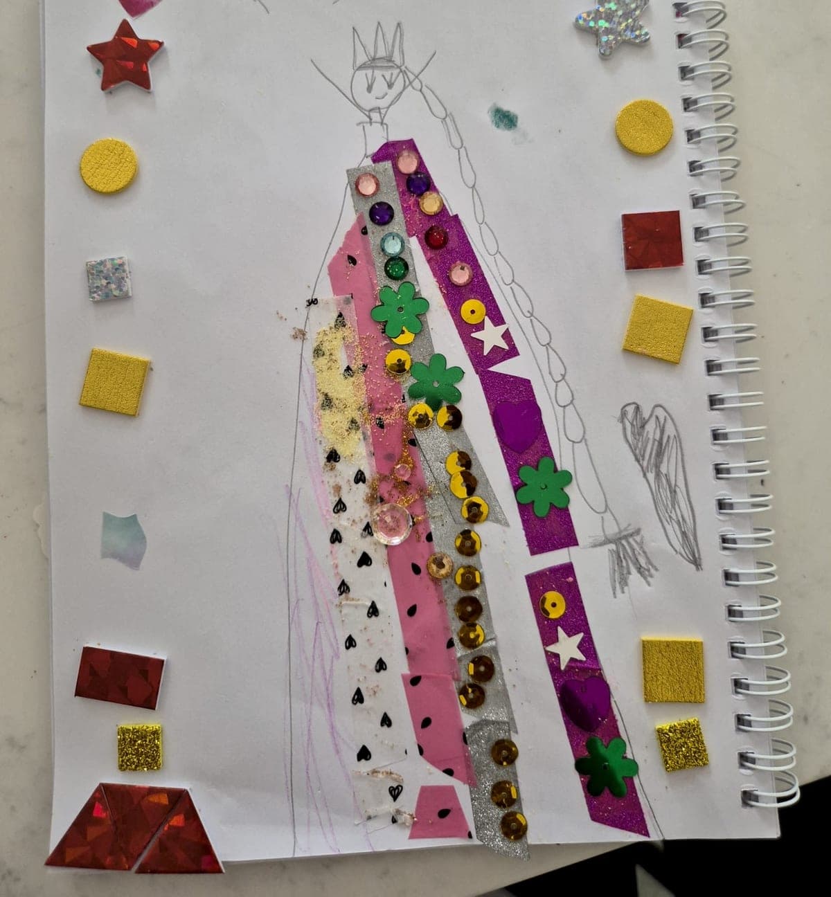 A phone photo of a child's drawing of a queen in a sequinned dress, taped and glittered onto a sketchbook page.